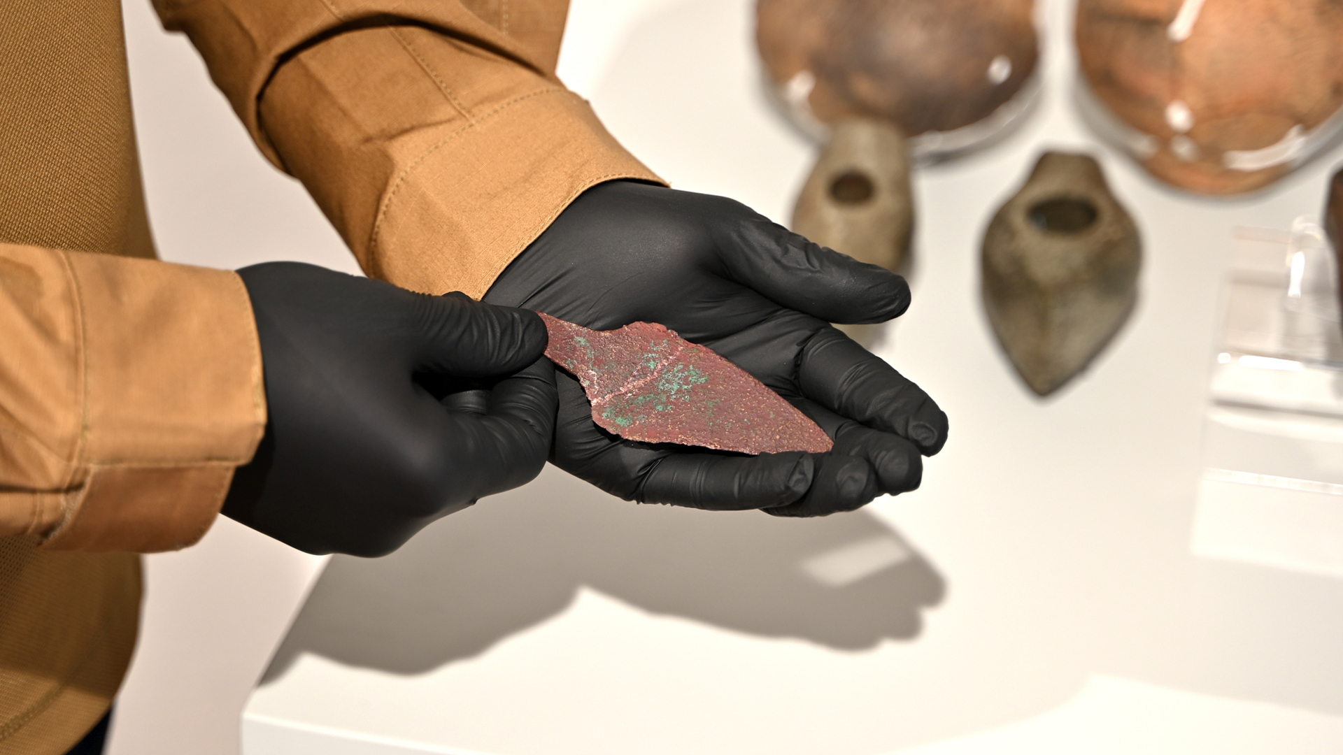 Badacz w czarnych rękawiczkach prezentuje miedziany sztylet mający ponad 4000 lat.