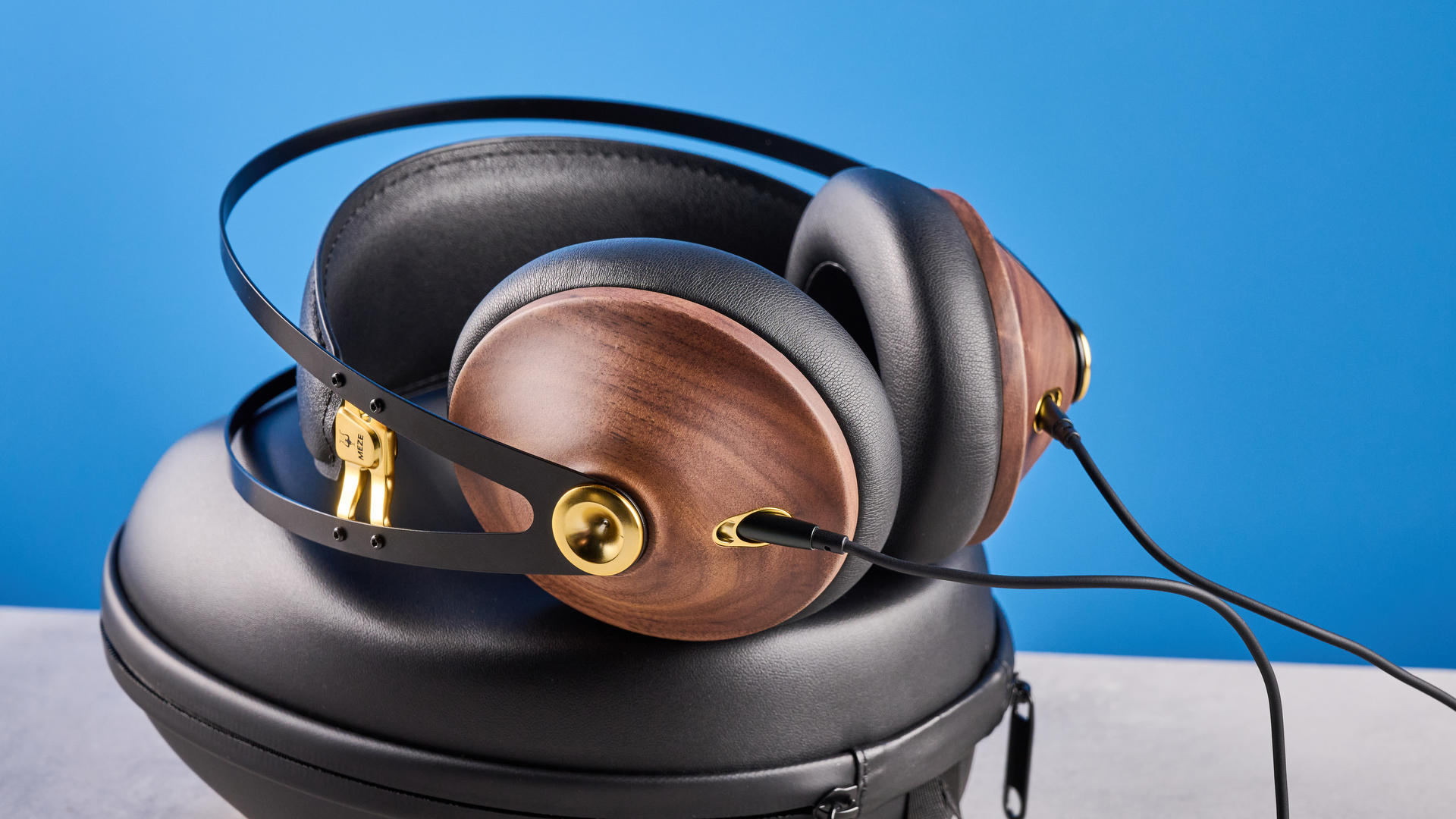 the meze 99 classics 2nd gen headphones with walnut finishes and gold touches against the blue tom&#039;s guide background