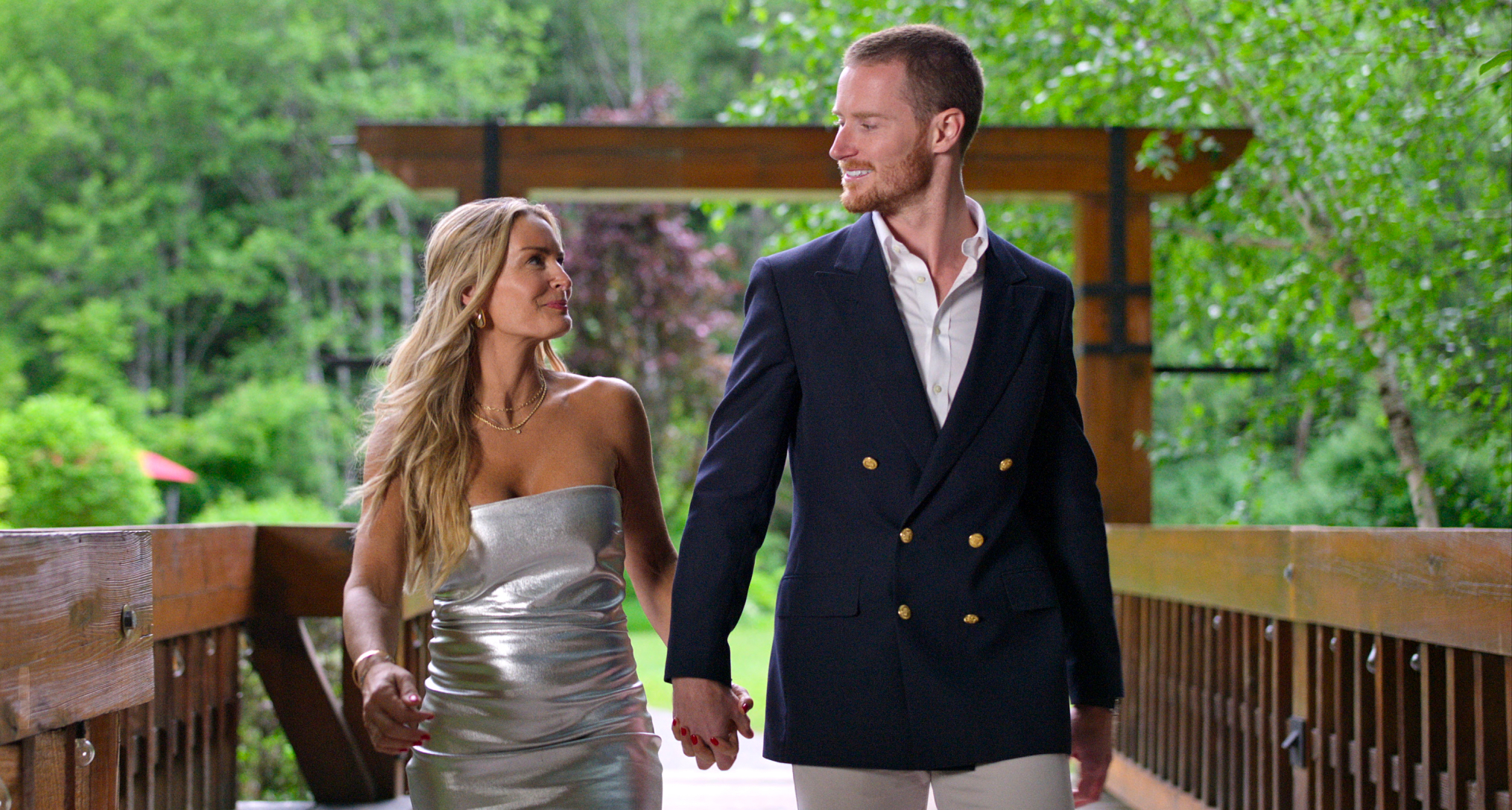 Theresa Demaria and John Merrill walk down a bridger wearing formal wear in a still from age of attraction