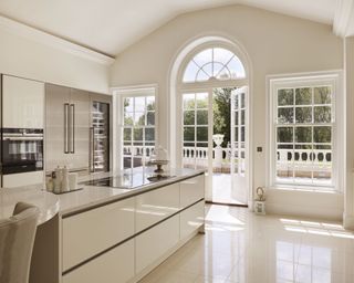 A grand white kitchen extension with an island and French doors leading out onto a terrace