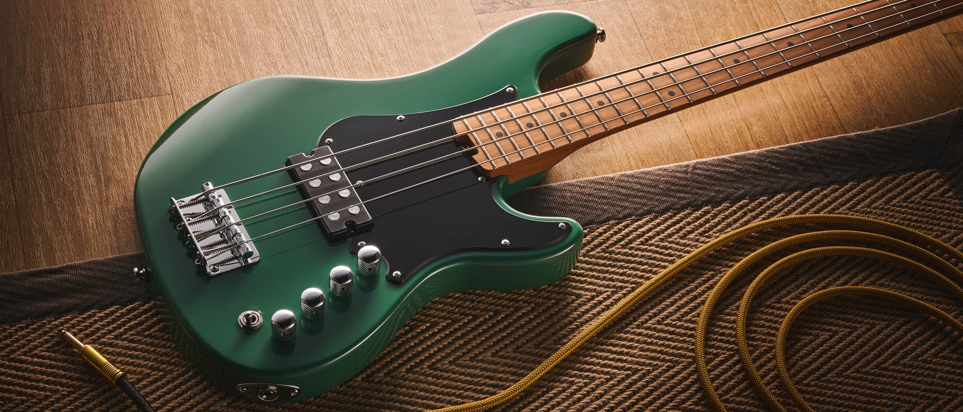 The Cort GB-Short Scale Bass finished in green, photographed against a light wooden floor and rug.