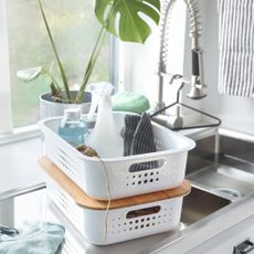 White stacking storage basket filled with cleaning products on top of kitchen sink