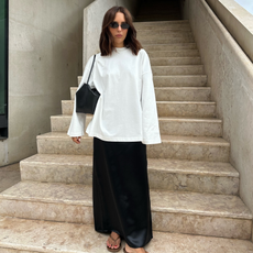 Influencer Débora Rosa wearing a white long sleeve t-shirt with a black maxi skirt and flip flops. 