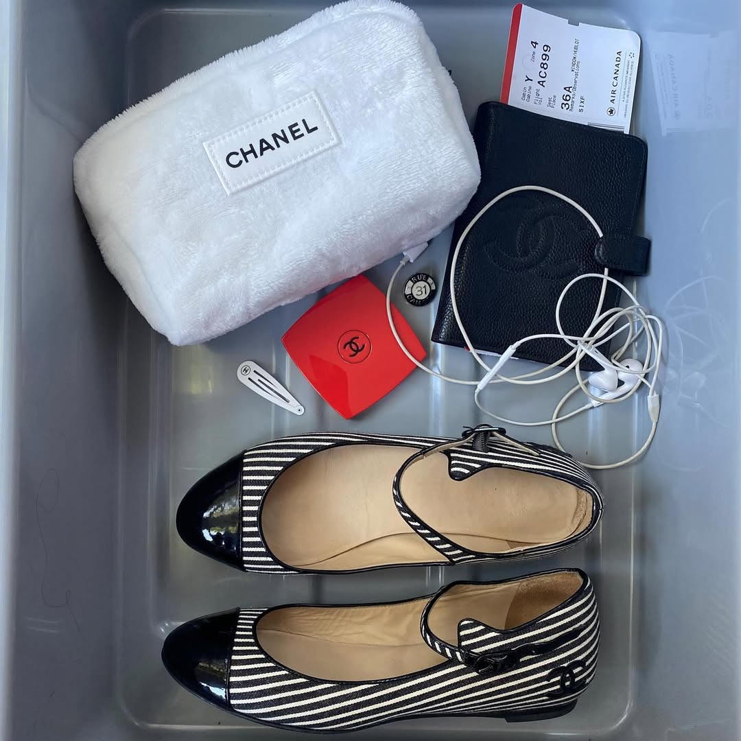 A flatlay of a pair of Chanel flats, a pouch, and a passport holder in an airport security bin.