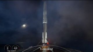 A black and white spacex falcon 9 rocket first stage sits on the deck of a ship at sea.