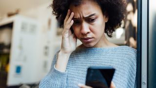 Woman looks anxiously at her phone with one hand on her forehead 