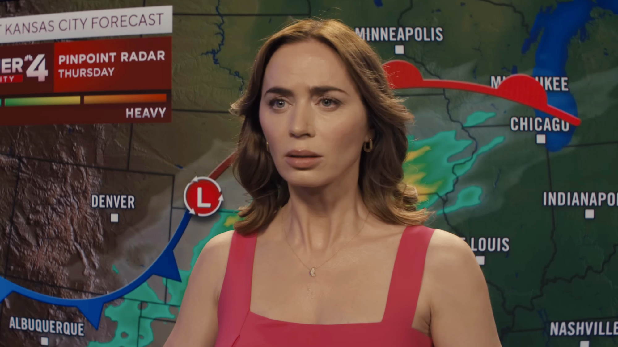 Emily Blunt in a red dress and giving a weather report in Disclosure Day.