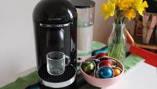 Bästa kapselmaskin: En Nespresso Vertuo Plus står på ett bord bredvid en skål med kaffekapslar, redo att brygga en kopp kaffe.