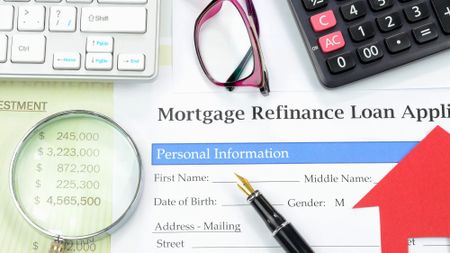 Application for mortgage refinance loan sitting on a table along with a calculator, keyboard, pen, and pair of glasses