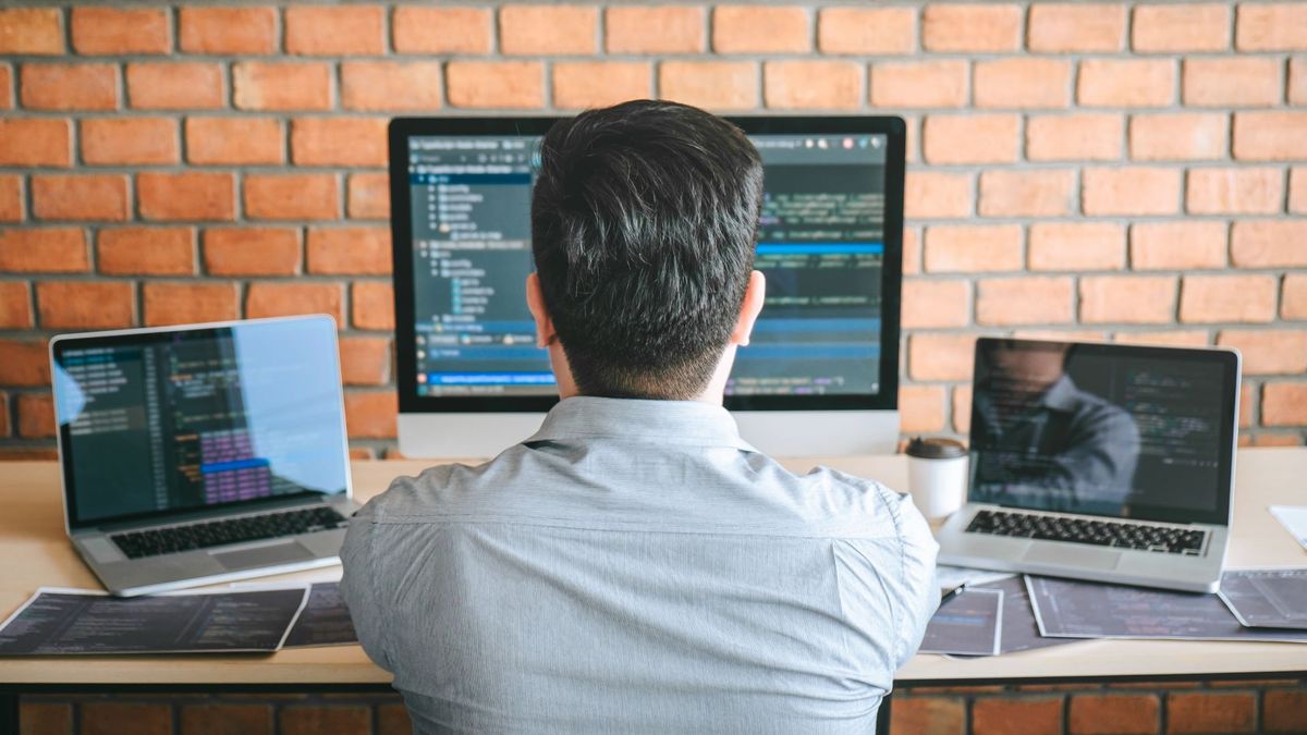 A person coding on a desktop computer and two laptops.