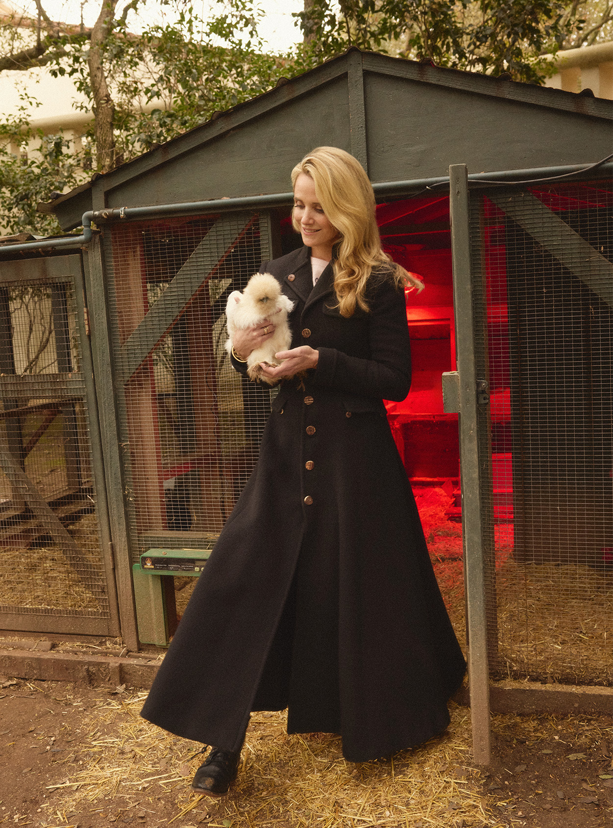 Jennifer Siebel Newsom holding a chicken outside a chicken coop
