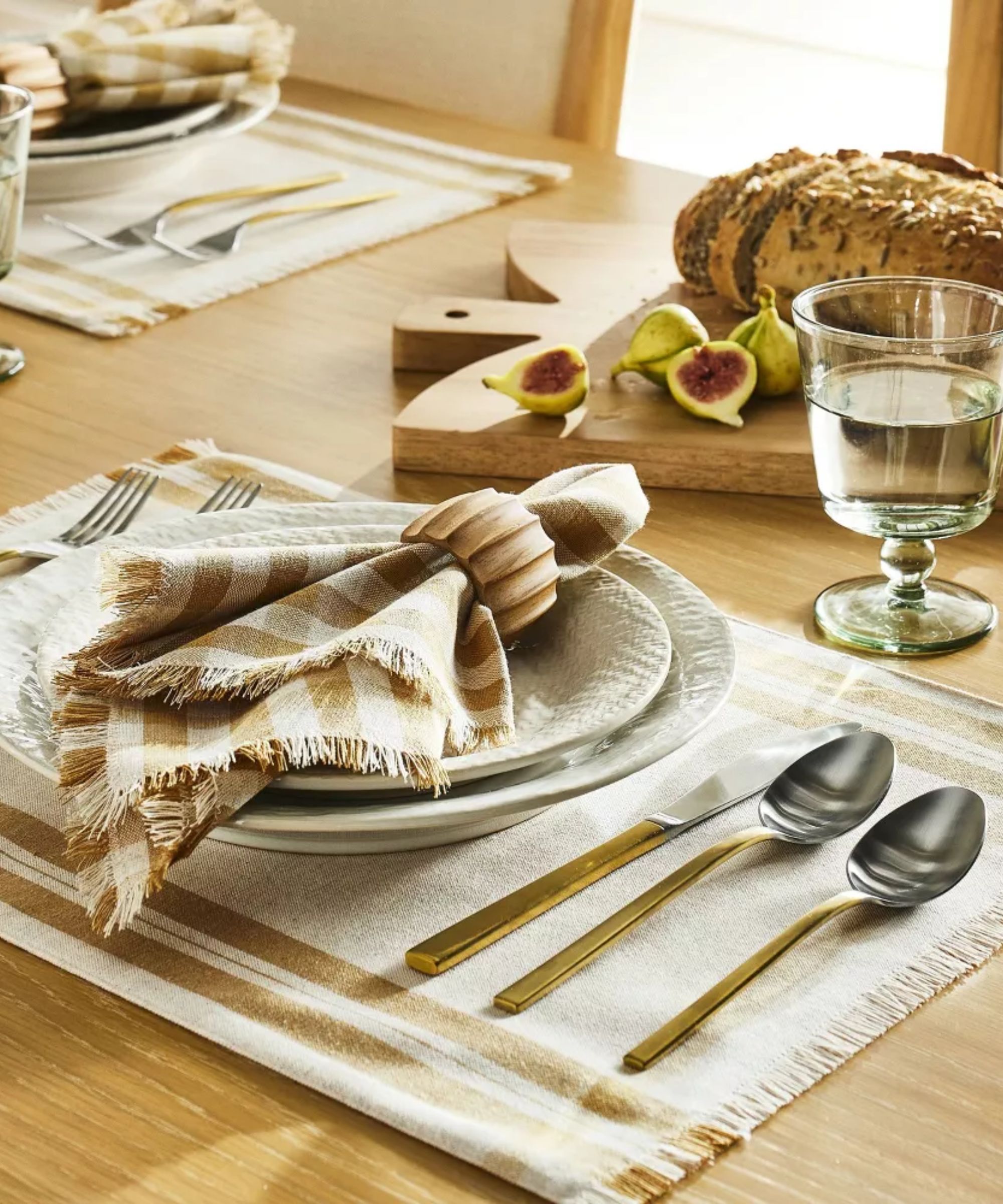 Pale wooden table with white placemats, beige and white gingham napkins, and two-tone cutlery