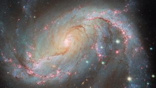 A giant spiral galaxy with spots of bright pink and dark reds in its arms.