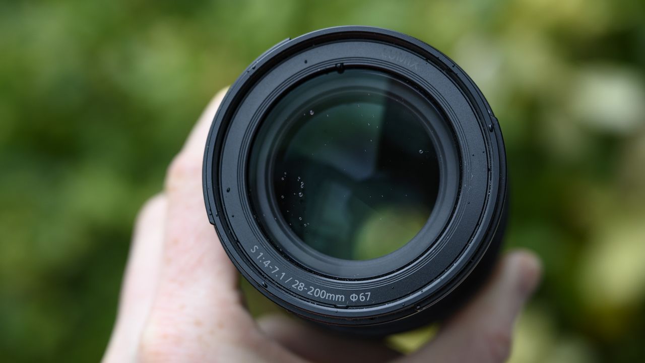 Panasonic Lumix S 28-200mm travel lens in the hand with leafy background and light rain