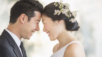 A young groom and bride touch foreheads and smile at each other.