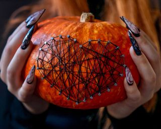 hands and pumpkin decorated with nails and threads close up.