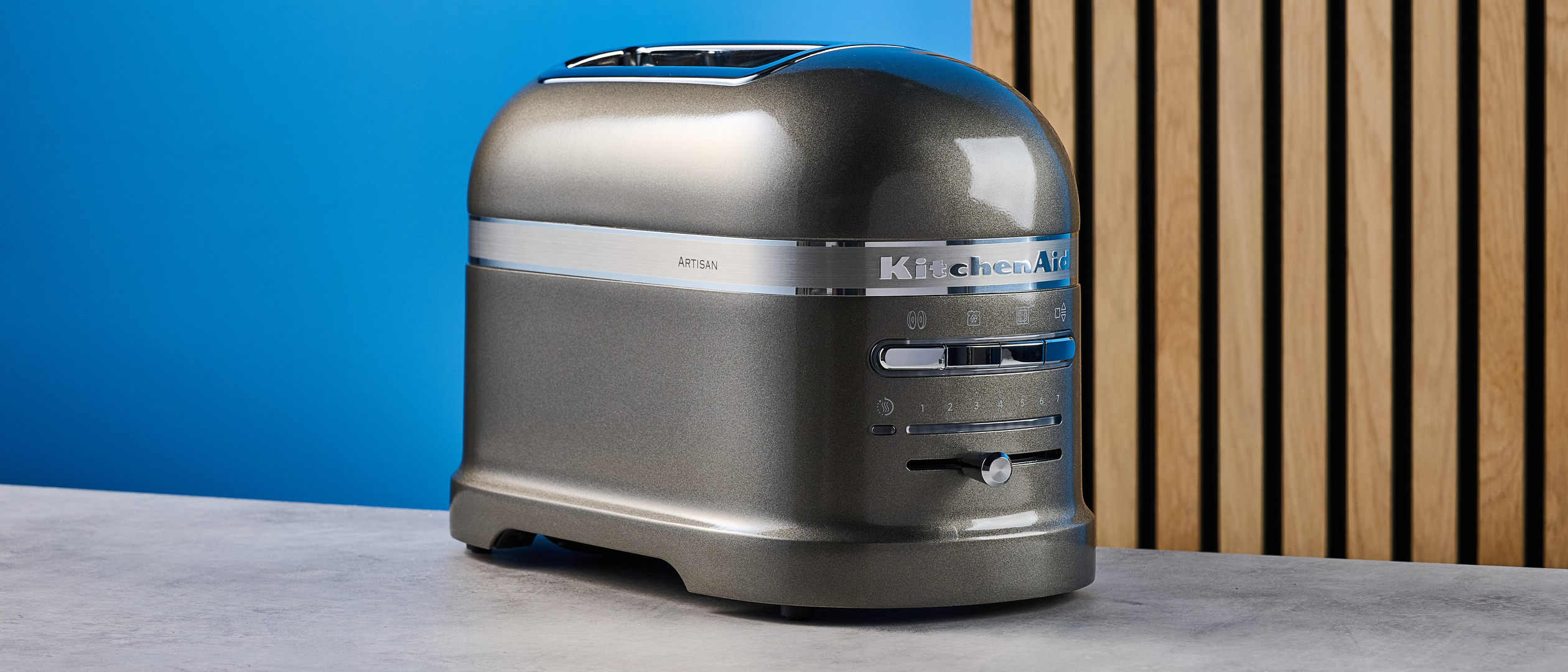 A photograph of the KitchenAid Pro Line toaster on a stone work surface with a blue and wooden background