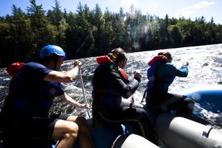 Three adults paddle a raft down a river in Maine