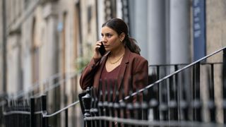 Lucie Shorthouse in a red jacket as DC Siobhan Clarke is on the phone by some railings in Rebus.