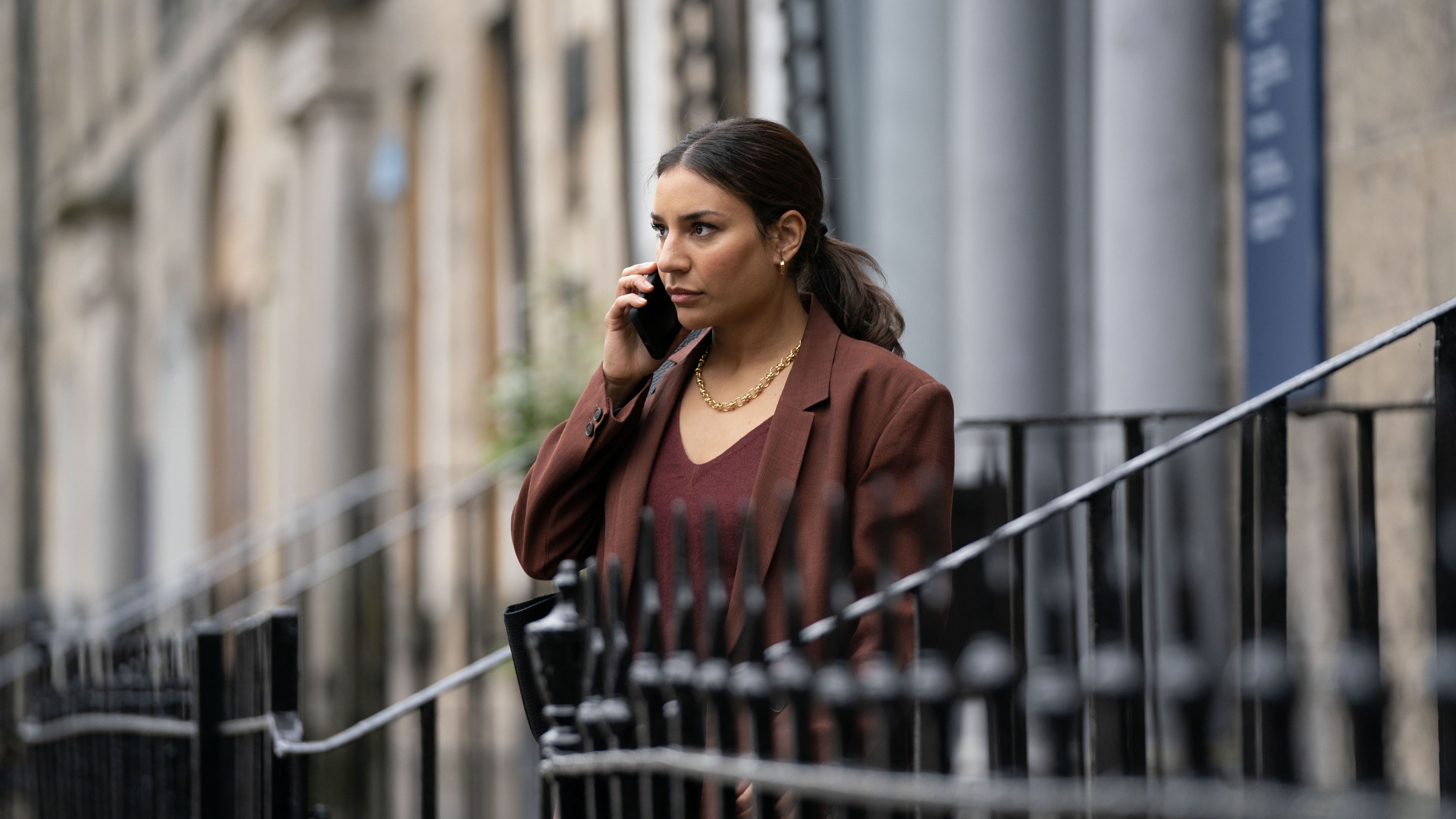 Lucie Shorthouse in a red jacket as DC Siobhan Clarke is on the phone by some railings in Rebus.