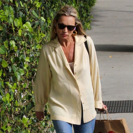 Kate Moss walks down the street wearing a butter yellow shirt with blue cuffed jeans and brown leather boots.