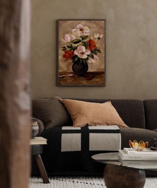 A dark living room with a framed floral picture and a brown couch