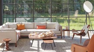 A modern living room with the back wall being entirely window. There is an off-white sectional and a wooden nesting coffee table. A cow print chair is in the corner