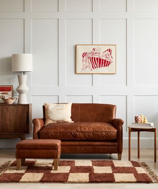 Brown leather sofa, checkered rug, ottoman foot stool, paneling