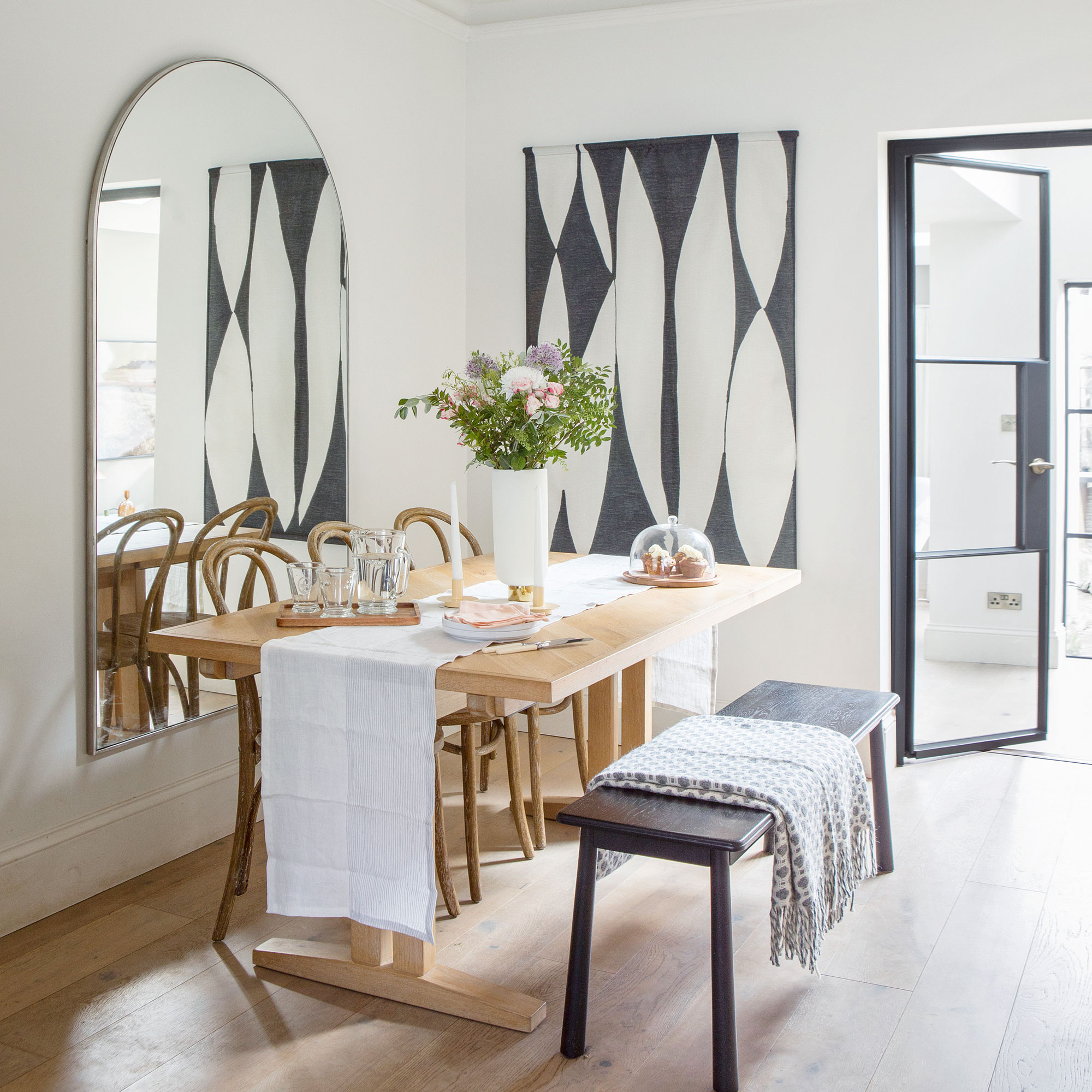 White dining room with a light wood table and large arch mirror on the wall