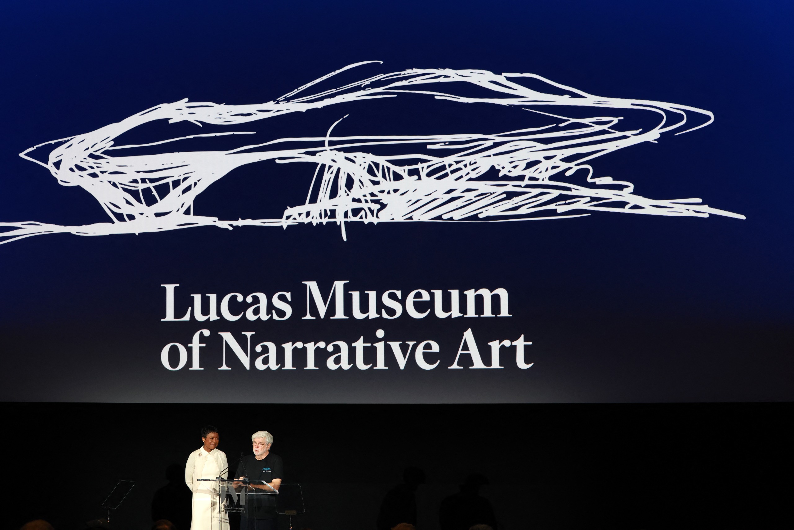 Two people stand in from of a large sign that reads Lucas Museum of Narrative Art