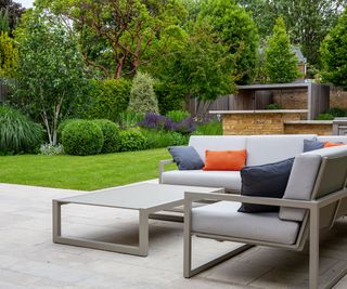 A modern light grey patio with corner sofa and lawn in the background