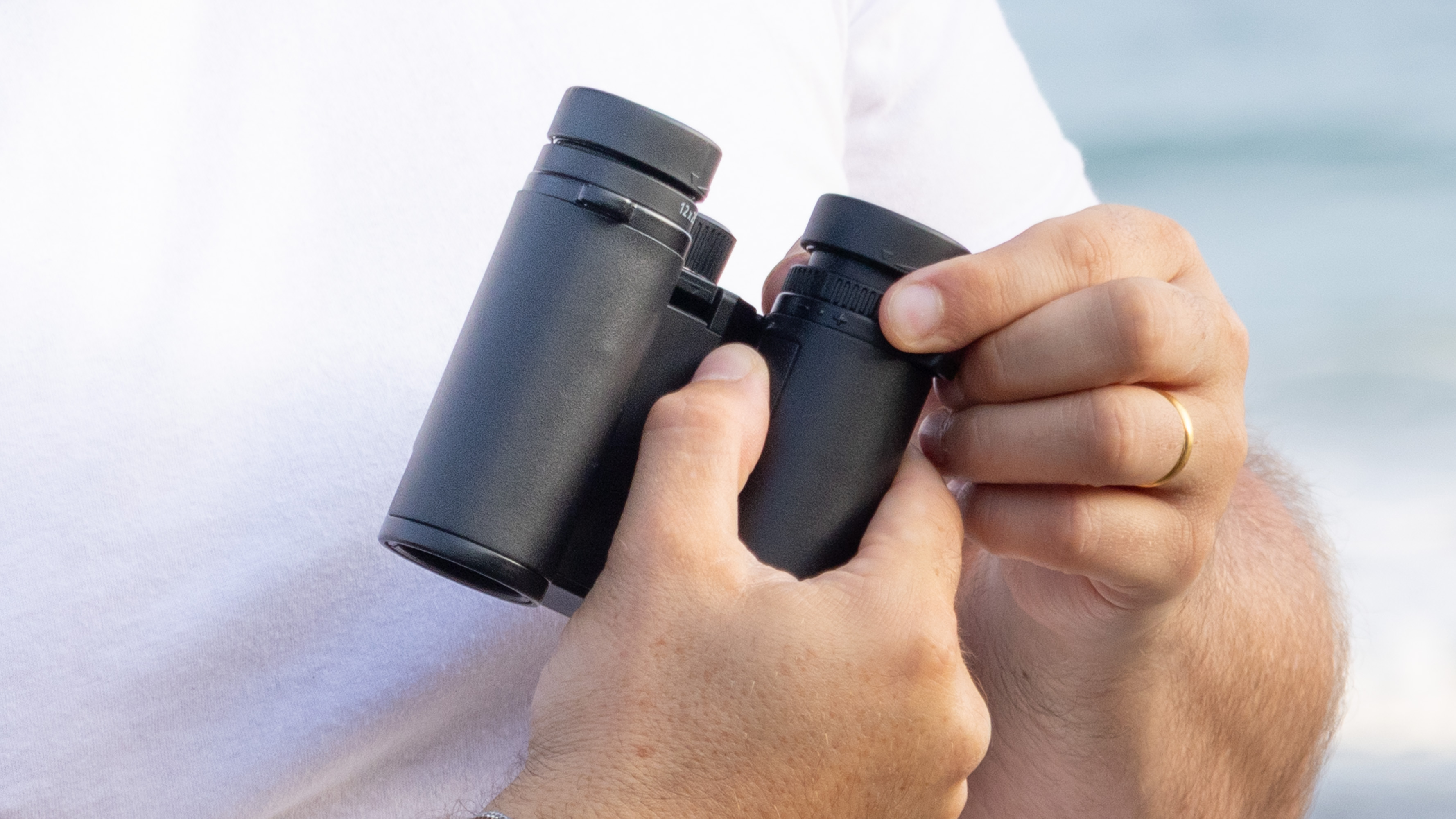 Nikon Stabilized 12x25 S binoculars held in the hands of the reviewer in front of breaking waves at the beach