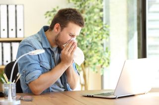 Man sneezing at his desk