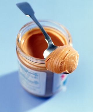 A jar of peanut butter with spoonful of contents on top of container