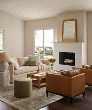 A white sofa and a tan armchair wither side of a wooden coffee table against white walls.