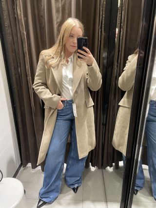 Woman wears beige coat, blue jeans and black heels