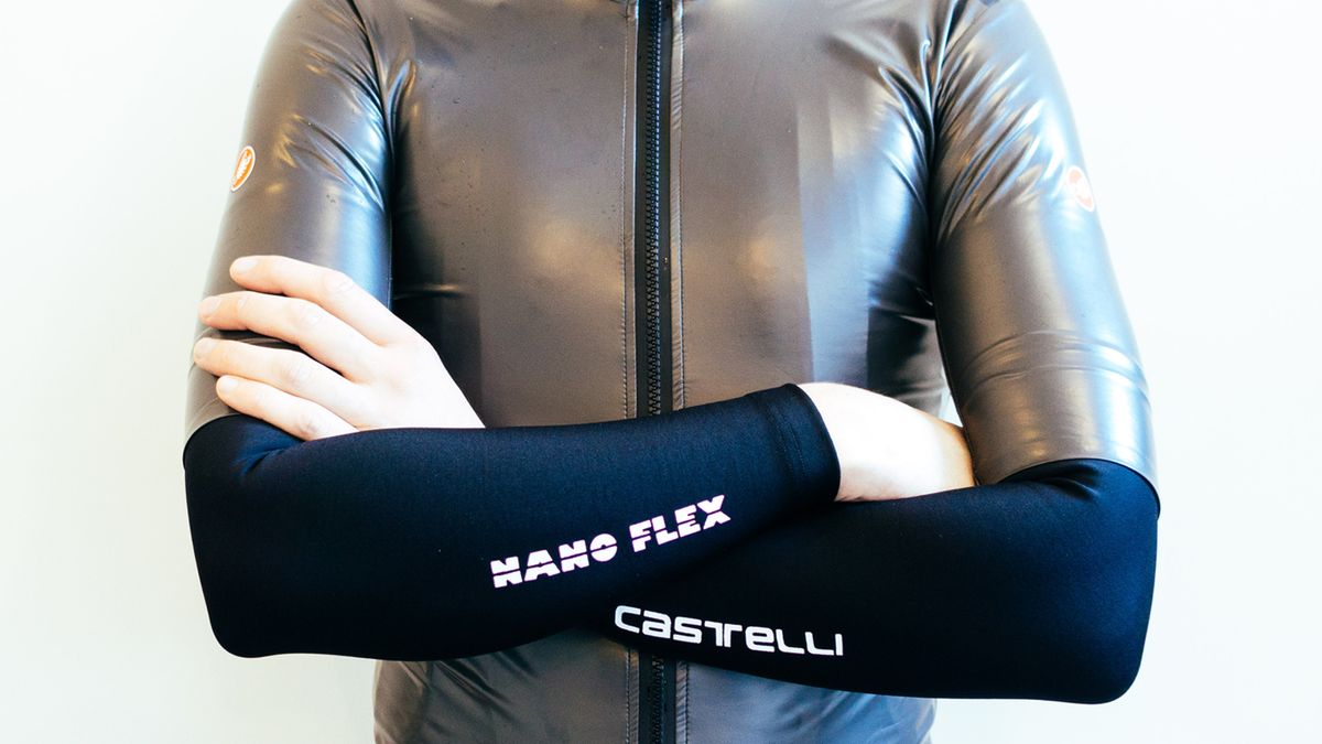 A man with his arms crossed wearing Castelli arm warmers against a white back ground