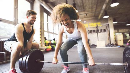 Young woman with training partner preparing to lift barbell in gym, working out with a partner