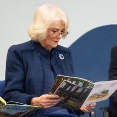 Queen Camilla wearing a blue coat reading a book