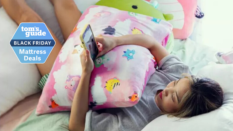 Woman holding a SquishPillow with a colorful pink cover while lying in bed looking at her phone