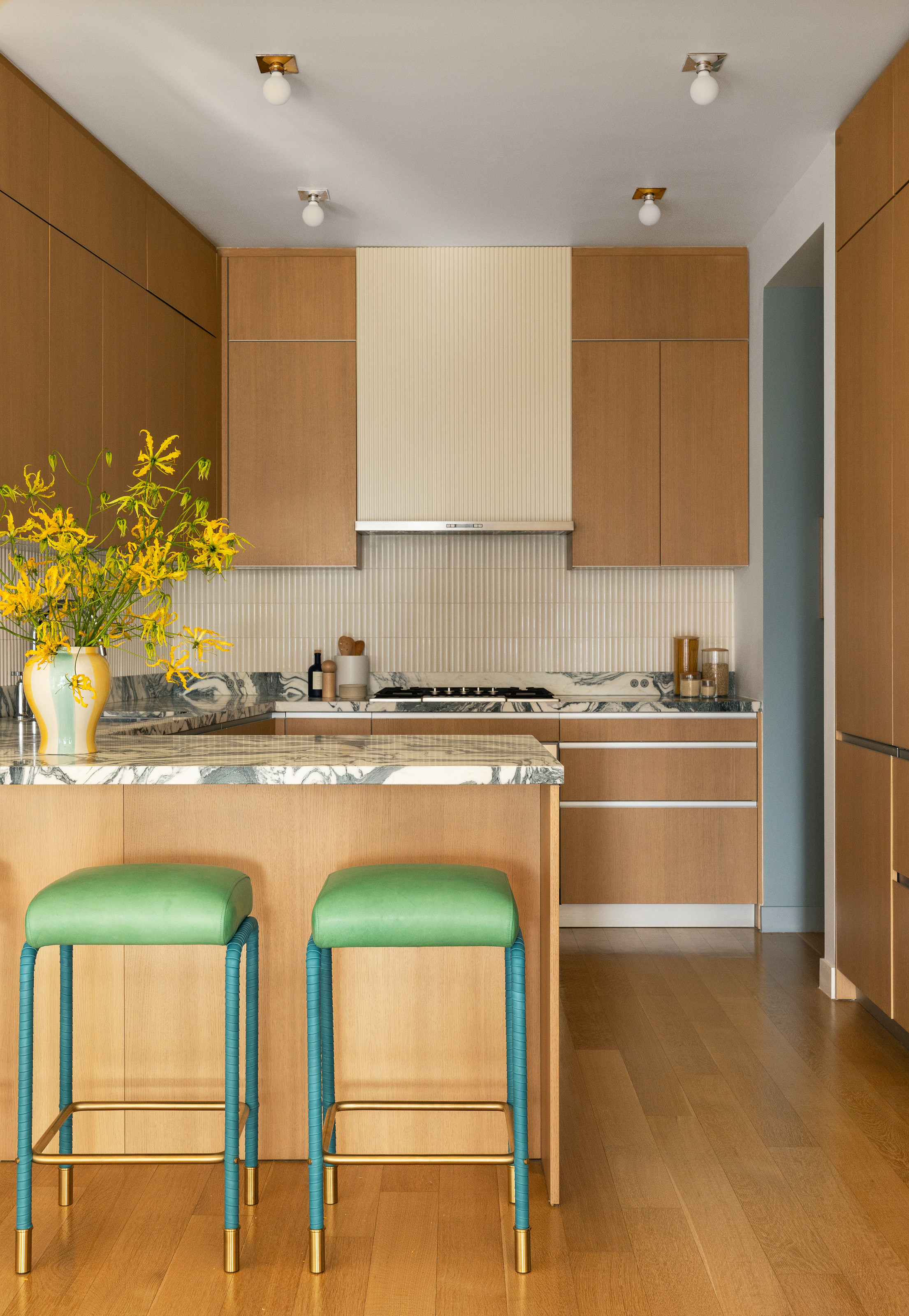 Oak kitchen with wrap-around bar area, green and blue bar stools and grey and white marble backsplash