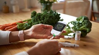 Young woman measuring her blood sugar using glucometer sitting at the table in living room.