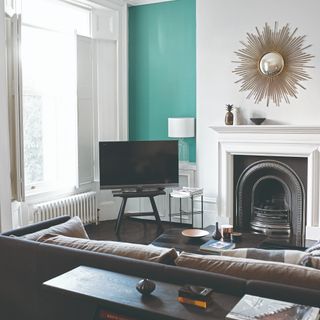 A living room with black fireplace and a sun-shaped mirror hanging above it with a TV on a stand in the corner