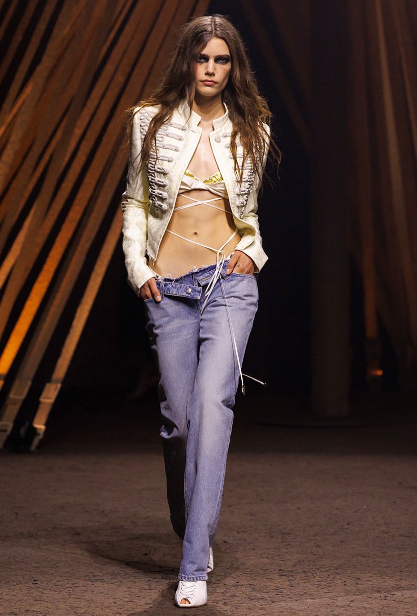 McQueen model wearing a Napoleon jacket with a bra top and low-rise jeans.