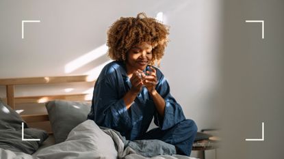 Woman wearing pyjamas sitting in bed holding a mug of tea and smiling after improving sleep hygiene