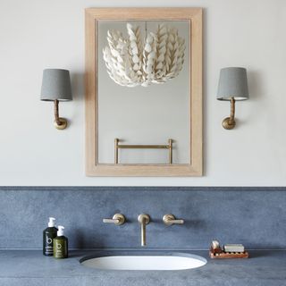 a neutral bathroom with a stylish washbasin and wall mounted taps and a simple mirros flanked by two shaded wall lights