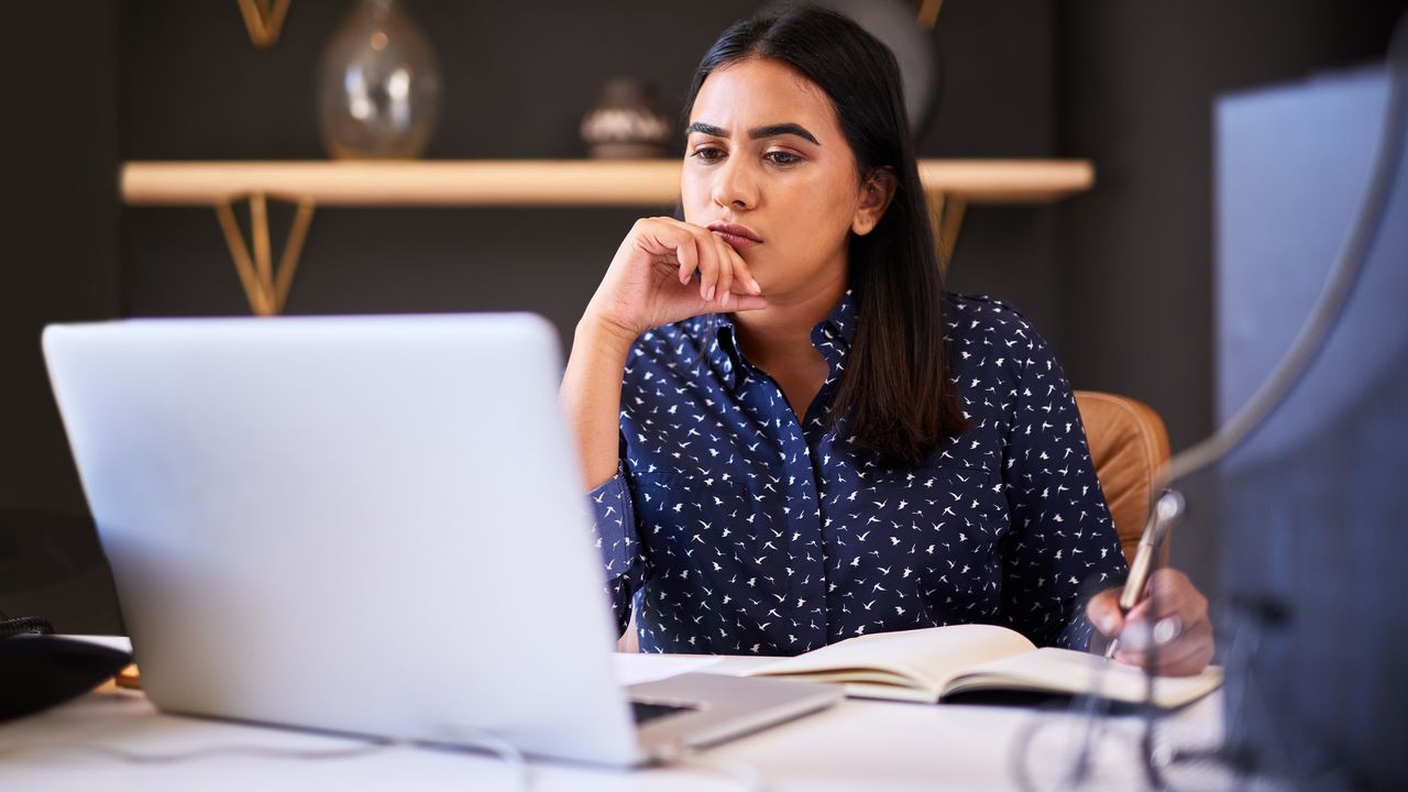 A woman looks intently at her laptop while sitting at a desk and doing research.