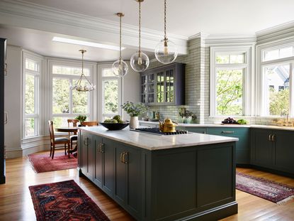 kitchen with blue island and wooden floor with red rugs with round dining table in background in bay window