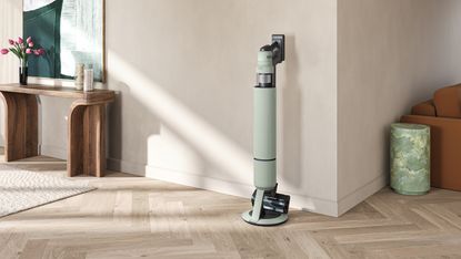Samsung Bespoke AI Jet Ultra cordless vacuum on satin mint cleaning station in minimalist room, in front of beige wall with chairs and side table