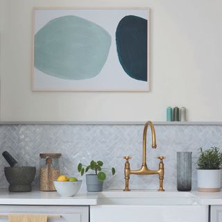 Kitchen with white sink, gold taps and art on wall.